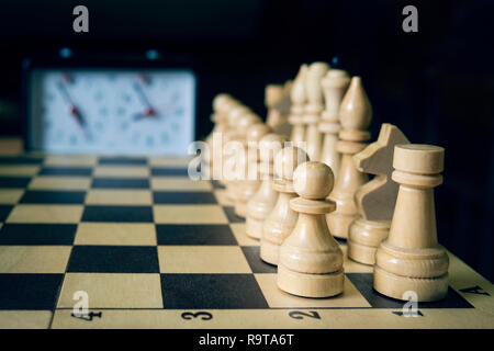Schachbrett mit Stücken und Uhr am Schreibtisch aus Holz in Verbindung mit dem Schachturnier, Wettbewerb. Beginn der Schach spiel. Stockfoto