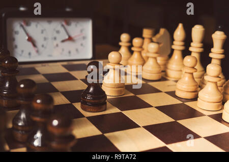 Alte Schachuhr auf dem Schachbrett mit Figuren, die Markierung in der Position bedeutet, läuft die Zeit auf dunklem Hintergrund Stockfoto