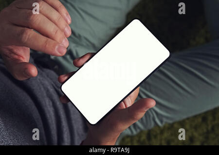 Eine slantwise Top-down-Sicht auf ein Junge über das Smartphone mit dem weißen Bildschirm Mann. Mann hält das Smartphone in der rechten Hand und bereit zu berühren, die Stockfoto