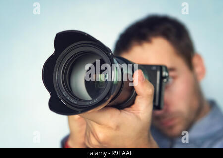 Männliche Fotografen halten Sie die Kamera in den Händen. Spiegellosen Kamera schließen sich in der Hand des jungen Mannes auf blauem Hintergrund. Der Reporter ein Bild aufnehmen. Stockfoto