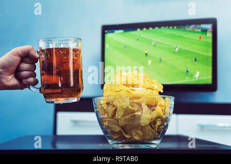 Bier Kartoffelchips und Sport im TV. Ein Mann wirft eine Tasse des dunklen Bier den Sieg seiner Mannschaft bei der Fußball-WM feiern. Gerade ein Fußball-ma Stockfoto