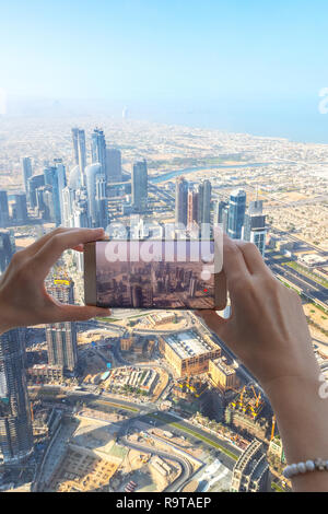 Nahaufnahme von Frau touristische Hand unter Foto von der Stadt Dubai mit Smartphone Kamera von Burj Khalifa Tower. Mädchen mit Handy auf Holi Stockfoto