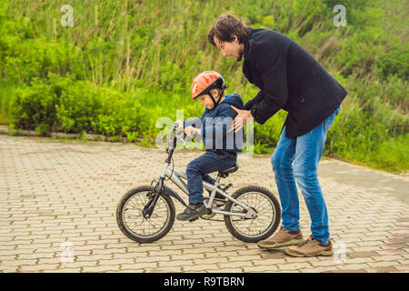 Vati lehrt Sohn ein Fahrrad im Park zu fahren Stockfoto