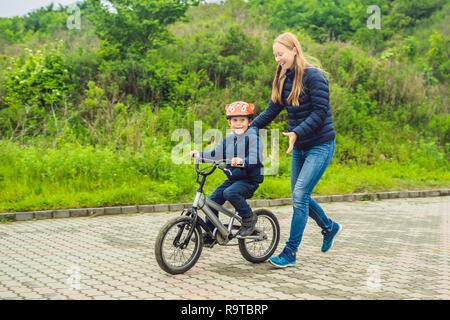 Mama lehrt Sohn ein Fahrrad im Park zu fahren Stockfoto