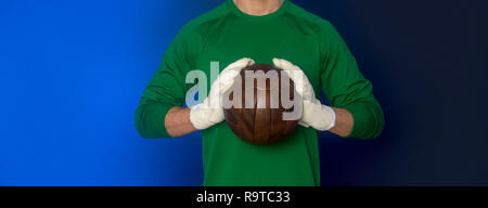 Fußball-Torwart halten alte Soccer Ball in Hand mit Handschuhen auf blauem Hintergrund Stockfoto