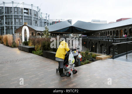 Rückansicht einer Frau und Kinderwagen mit Einkaufstaschen und Gasholders Apartment Gebäude und Kohle Tropfen Yard Kings Cross London UK KATHY DEWITT Stockfoto