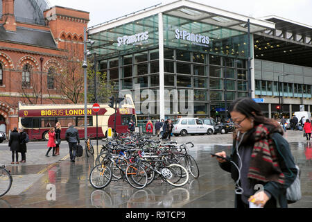 Frau, die ihr Mobiltelefon mit geparkten Fahrrädern außerhalb der geschäftigen Stadtstraße ansieht, Gebäude am Bahnhof St Pancras Kings Cross in Rain London, Großbritannien, KATHY DEWITT Stockfoto