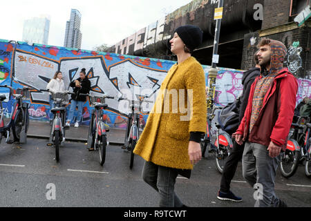 Die Leute, die Brick Lane East End junge Frau tragen gelbe Fell die Straße entlang bummeln in Winter in Shoreditch East London E1 UK KATHY DEWITT Stockfoto