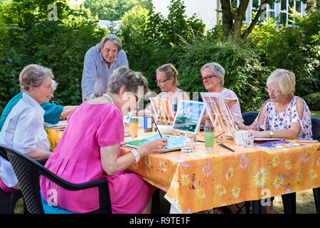 Älteren Damen die Kunst Unterricht im Freien sitzen am Tisch und malen Bilder, folgenden männliche Lehrer. Stockfoto