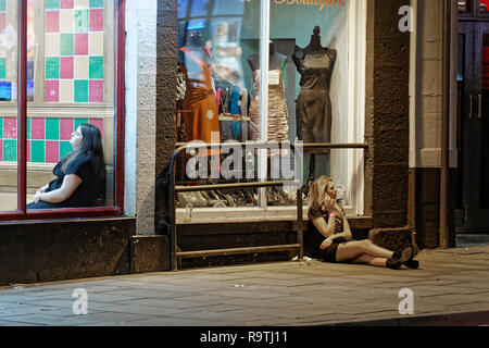 Im Bild: Eine Frau sitzt auf dem Bürgersteig. Freitag, 14 Dezember 2018 Re: Nachtschwärmer in der Wind Street, Swansea, Wales, UK. Stockfoto