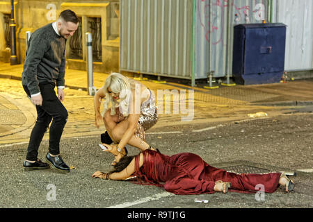 Im Bild: Eine Frau ist zu ihren Füßen, die von einem Mann und einer Frau geholfen. Freitag, 14 Dezember 2018 Re: Nachtschwärmer in der Wind Street, Swansea, Wales, UK. Stockfoto