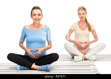Zwei schöne schwangere Frauen halten sich an den Händen im Herzen anmelden Bäuche isoliert auf weißem Stockfoto