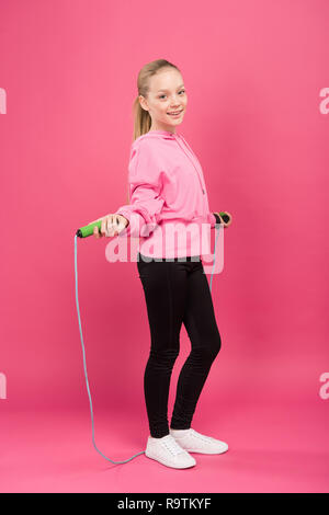 Glückliches Kind in Sportkleidung Training mit Springseil, isoliert auf Rosa Stockfoto