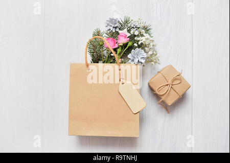 Weihnachten mockup Shopping Konzept. Kraft Paket mit Holz- tag und xmas Dekor Tannenzweigen, Rosen, Kegel mit Platz für Ihren Text Stockfoto