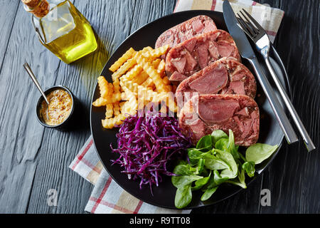 Geschnetzeltes Rindfleisch Zunge Aspik mit Pommes frites, grüne Blätter und Rotkohl Salat auf einem schwarzen Schild an einem hölzernen Tisch serviert mit Senf in eine Schüssel geben, Anzeigen Stockfoto