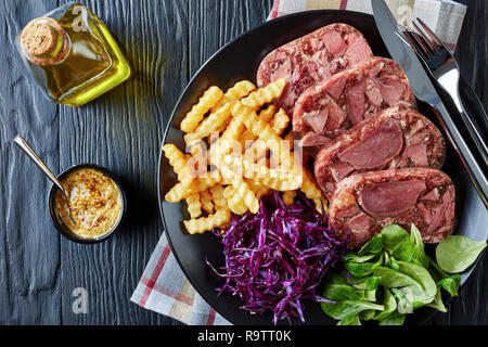 Ansicht von oben der Geschnetzeltes Rindfleisch Zunge Aspik mit Pommes frites, grüne Blätter und Rotkohl Salat auf einem schwarzen Schild auf einem Holztisch serviert mit mustar Stockfoto