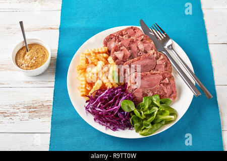 Geschnetzeltes Sülze rind Zunge mit Pommes frites, grüne Blätter und Rotkohl Salat auf einem weißen Teller auf einen hölzernen Tisch serviert mit Senf in einer Schüssel, vi Stockfoto