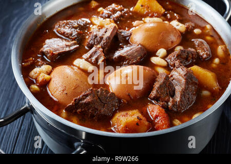 In der Nähe der traditionellen jüdischen Cholent Hamin - Hauptgericht für den Schabbat Mahlzeit, langsam gekochtes Rindfleisch mit Kartoffeln, Bohnen und braune Eier in einem Topf auf einem schwarzen Stockfoto