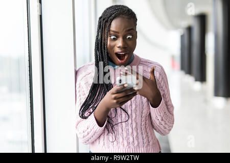 Junge überrascht afro Frau lesen Nachricht vom Telefon vor panoramafenster Stockfoto