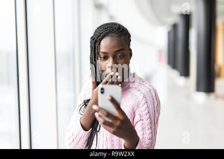 Junge überrascht afro Frau lesen Nachricht vom Telefon vor panoramafenster schockiert Stockfoto