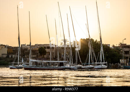 Sonnenuntergang Nil Assuan der West Bank mit kleinen Dorf Häuser mit Angeln Segeln Boote felucca. Stockfoto