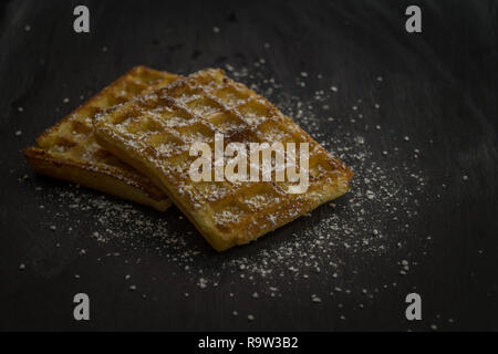 Leckere hausgemachte belgische Waffeln auf einem schwarzen Platte. Dessert mit Puderzucker. Stockfoto
