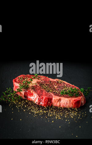 Raw trockenen Jahren Entrecote Steak. Köstliche barbecure Rib Eye Steak mit verschiedenen Gewürzen auf einem dunklen Stein Platte. Stockfoto