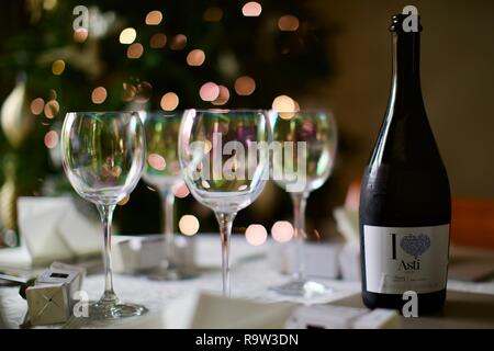 Weingläser und eine Flasche Asti mit Weihnachtsbeleuchtung im Hintergrund Stockfoto