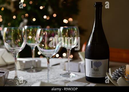 Weingläser und eine Flasche Asti mit Weihnachtsbeleuchtung im Hintergrund Stockfoto
