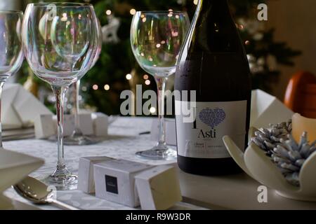 Weingläser und eine Flasche Asti mit Weihnachtsbeleuchtung im Hintergrund Stockfoto