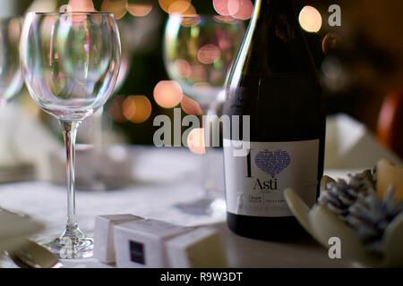 Weingläser und eine Flasche Asti mit Weihnachtsbeleuchtung im Hintergrund Stockfoto