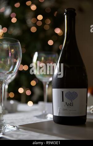 Weingläser und eine Flasche Asti mit Weihnachtsbeleuchtung im Hintergrund Stockfoto