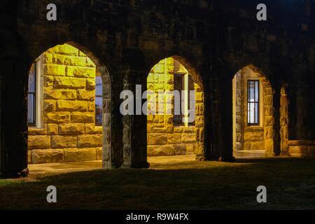 Nächtlicher Blick von außen von einem schwach gewölbten Durchgang der Heiligen Kapelle an der Universität im Süden in Sewanee, Tennessee beleuchtet. Stockfoto