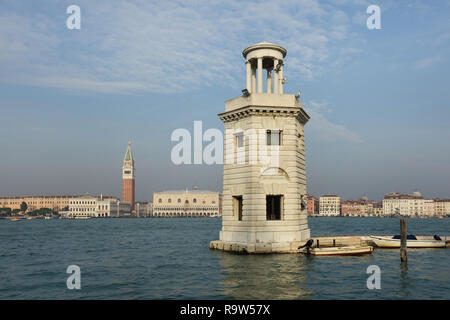 Leuchtturm auf der Insel San Giorgio Maggiore in der venezianischen Lagune (Laguna di Venezia) in Venedig, Italien. Der Dogenpalast (Palazzo Ducale) und St Mark's Campanile (Campanile di San Marco) werden im Hintergrund gesehen. Stockfoto