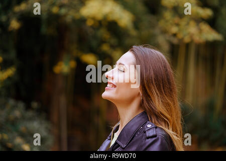 Seitenansicht der glückliche junge Dame die Augen geschlossen halten und Lächeln beim Stehen auf unscharfen Hintergrund der park Bäume Stockfoto