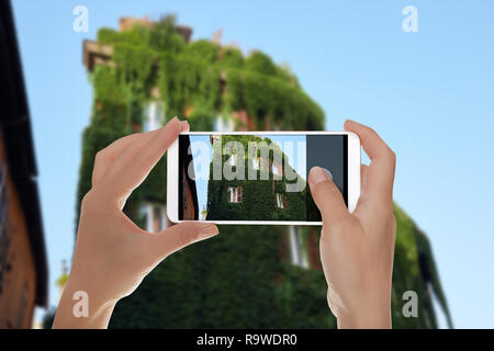 Ein Mann macht ein Foto von dem Gebäude ist komplett mit Rebe vorsichtig in Trastevere, Rom, Italien, und auf einem Mobiltelefon überwachsen Stockfoto