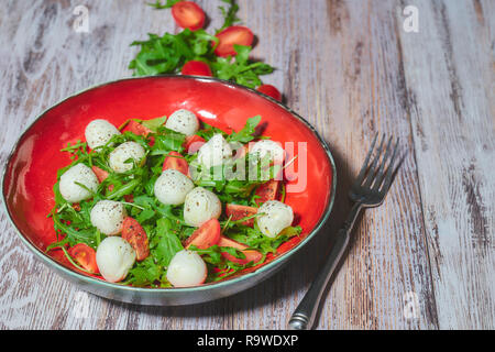 Frischer Salat mit Ruccola, Tomaten, Mozzarella Käse auf einem weißen, schäbig, Holztisch. vertikale Ansicht. Kopieren Sie Platz. Stockfoto