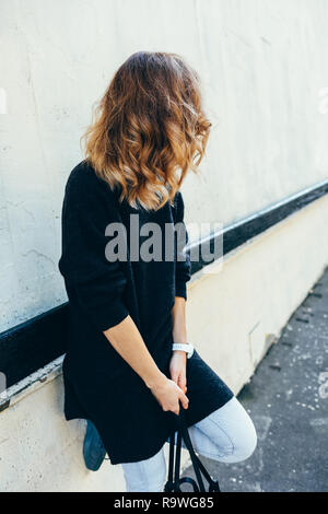 Junge Frau mit blondem Haar flatterte neben Gebäudewand, stützte sich auf Geländer und beiseite. Candid lifestyle Foto unkenntlich. Stockfoto