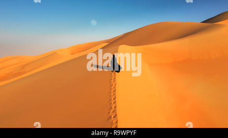 Luftaufnahme von einer Drohne neben einer Frau in Abaya (Vereinigte Arabische Emirate traditionelles Kleid) zu Fuß auf den Dünen in der Wüste von den leeren Quar fliegen Stockfoto