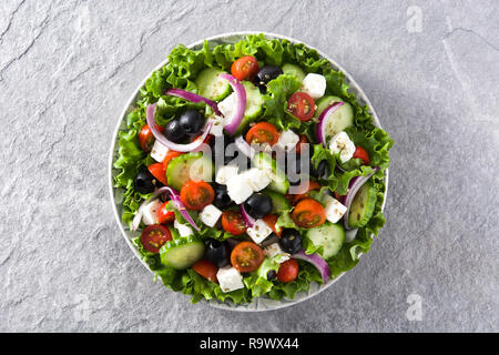 Griechischer Salat frisch in der Platte mit schwarzen Oliven, Tomaten, FETA-Käse, Gurken und Zwiebeln auf grauem Hintergrund. Ansicht von oben. Stockfoto