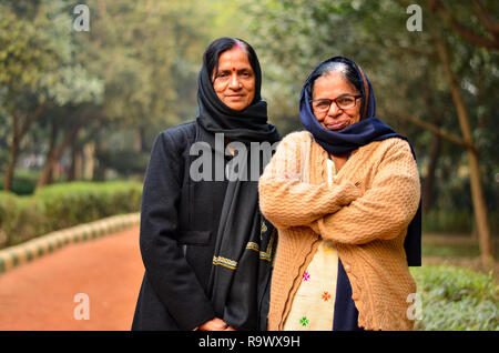 Zwei älteren indischen Freundinnen, Schwestern, Frauen, die in einem Park tragen Pullover, Schal, Stola & Mäntel mit gekreuzten Händen während der Winter in Delhi, Indien Stockfoto
