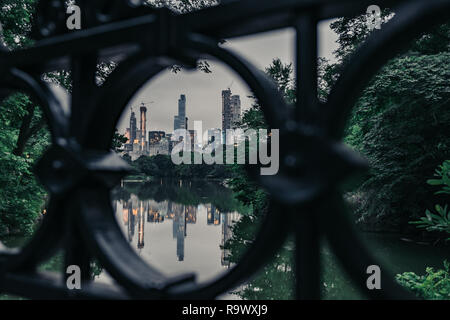 Skyline von New York City durch einen schwarzen Kreis eiserne Geländer einer Brücke im Central Park mit Wasser Reflexionen in der Dämmerung Stockfoto