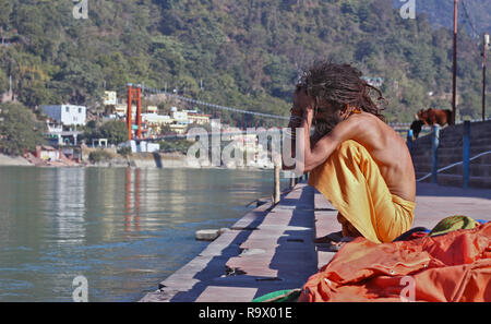 Eine junge Naga Sadhu mit Skinny Körper und Dreadlocked Haar am Ufer des heiligen Flusses Ganges, Rishikesh, Uttarakhand, Indien sitzen Stockfoto