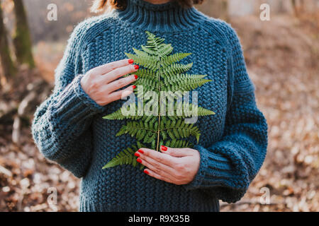 Frau in Pullover holding Farn Blatt Stockfoto