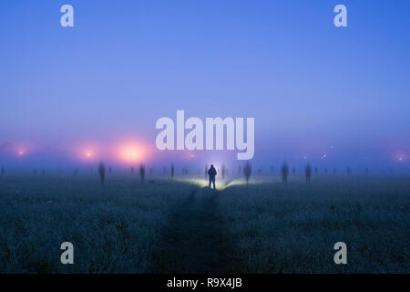 Eine einsame Gestalt mit einer Taschenlampe in einem Feld als geisterhaft verschwommene Figuren auf eine gespenstische, nebligen Nacht. Stockfoto