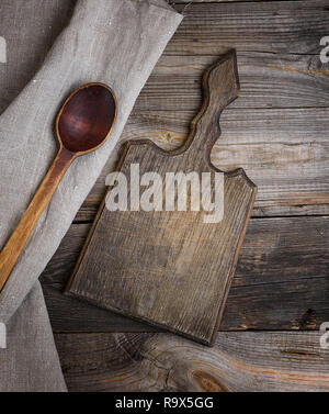 Alte braune Holzlöffel und Schneidbrett auf einer hölzernen Hintergrund, neben einem grauen Handtuch, Ansicht von oben Stockfoto