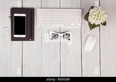 Wireless Slim Keyboard und Maus, Smartphone, Notepad, Gläser, Blumen auf weißem Holz- Hintergrund Stockfoto