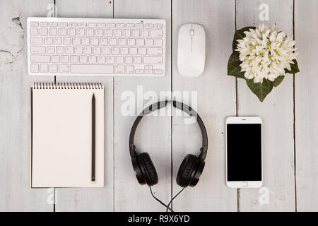 Wireless Slim Keyboard und Maus, Smartphone, Notepad, Kopfhörer und Blumen auf weißem Holz- Hintergrund Stockfoto