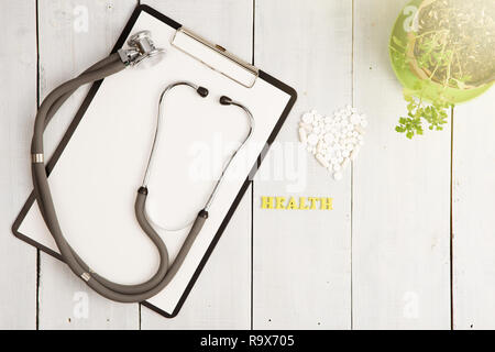 Medizinisches Konzept - Stethoskop, pad, Flasche, Weiß Herz von Pillen und Kapseln, Gesundheit Beschriftung auf weißem Schreibtisch aus Holz Stockfoto
