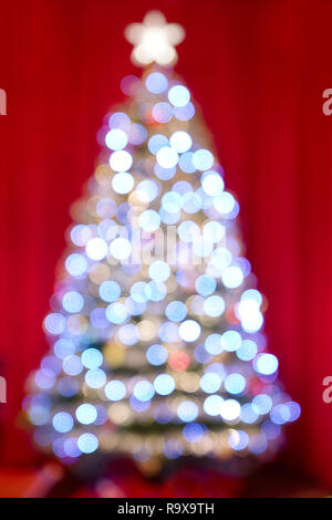 Weihnachtsbaum und Lichter aus Bild unscharf Kugeln und Dekorationen mit Lametta gegen roten Hintergrund Vorhänge farbenfrohe Bokeh Stockfoto